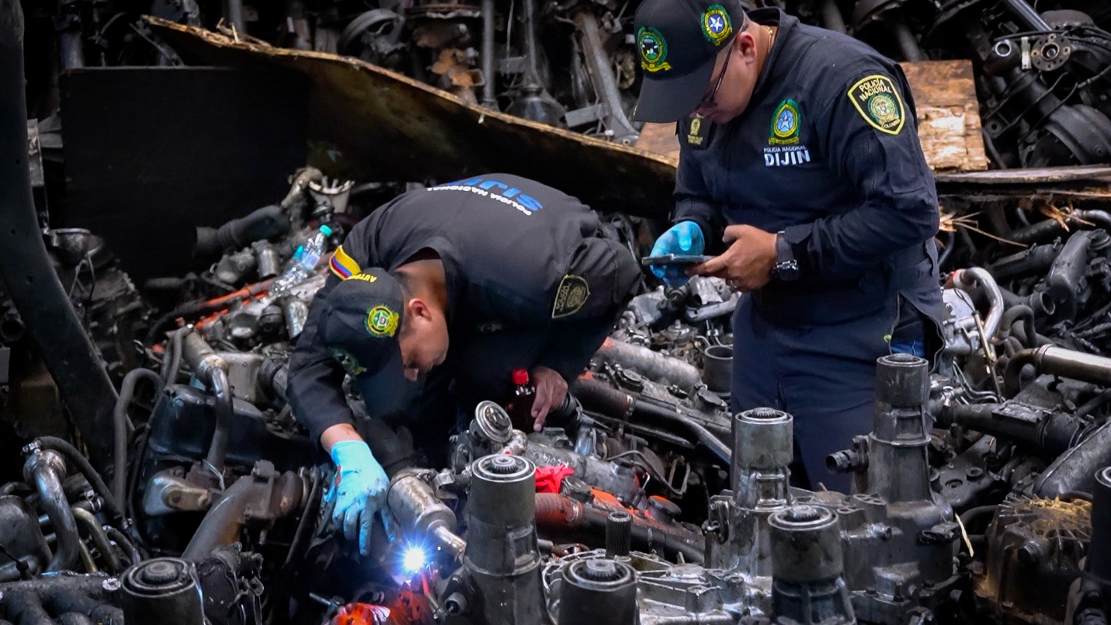 Capturados, motores incautados y establecimientos sellados: así fue el megaoperativo en zona de autopartes en Los Mártires Dos hombres revisando de cerca autopartes